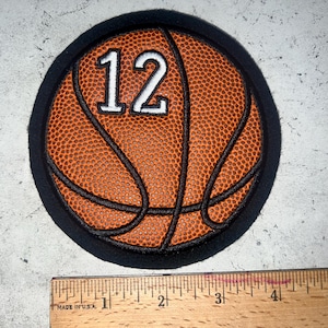May include: A round patch featuring a basketball design with the number 12 in white. The basketball is orange with black lines and a textured surface, set against a black background. A ruler is at the bottom.