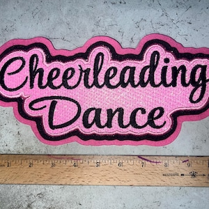 May include: Pink felt patch with black embroidered text that reads "Cheerleading Dance".