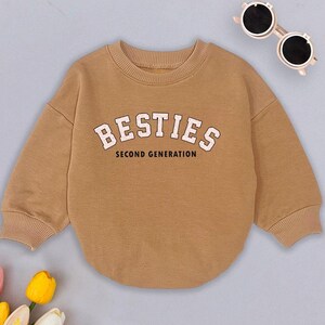May include: A brown sweatshirt with the text "BESTIES SECOND GENERATION" in pink and black lettering.