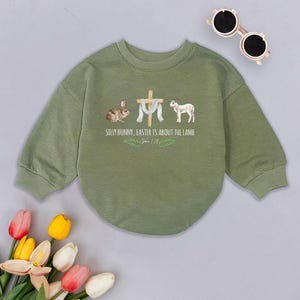 May include: Green long-sleeved sweatshirt with a graphic of a bunny, a cross, a lamb, and the text "Silly Bunny, Easter is about the Lamb, John 1:29".