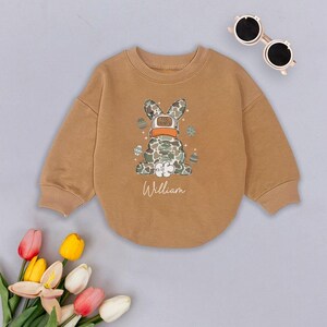 May include: A brown sweatshirt with a camouflage bunny wearing a hat that says "I'm bunny" and the name "William" printed on the front.