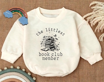May include: A white long-sleeved onesie with the text "the littlest book club member" and a black and white illustration of a stack of books with butterflies and flowers.