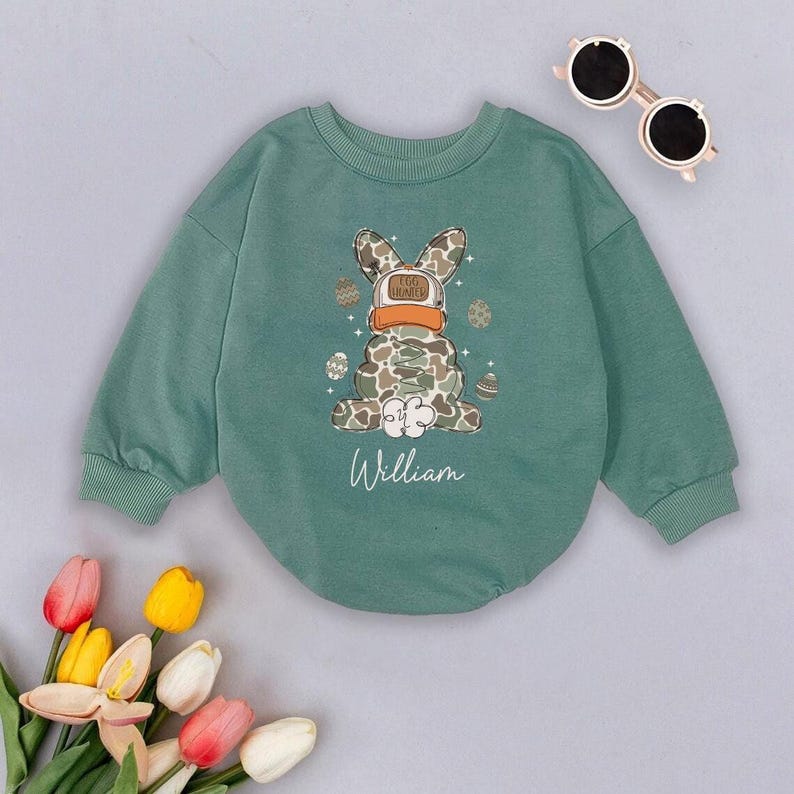 May include: Green long-sleeved sweatshirt with a cartoon bunny wearing a hat that says "Egg Hunter" and holding Easter eggs. The sweatshirt has the name "William" printed below the bunny.