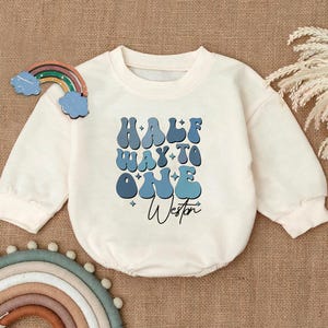 May include: A white baby onesie with a blue and white graphic that says "HALF WAY TO ONE" with the name "Weston" written underneath.