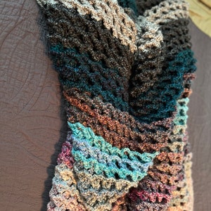 May include: A multi-colored crocheted blanket with a textured pattern. The blanket is made with a variety of shades of blue, brown, gray, and pink yarn.