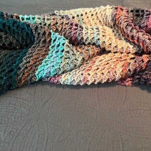 May include: A multi-colored crocheted throw blanket with a textured pattern. The blanket is made of a soft, yarn and features shades of teal, brown, purple, and gray.