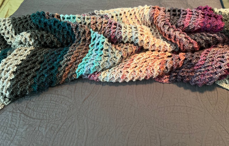 May include: A multi-colored crocheted throw blanket with a textured pattern. The blanket is made of a soft, yarn and features shades of teal, brown, purple, and gray.