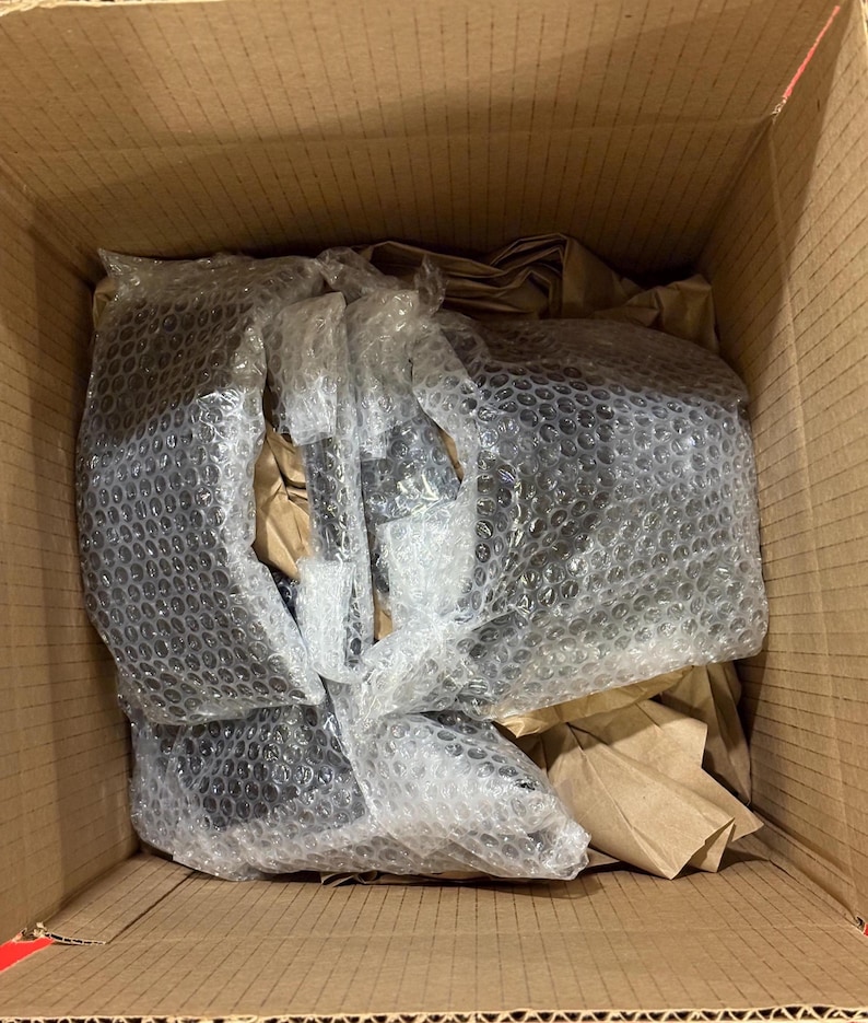 Pode incluir: Uma caixa de cart&atilde;o aberta contendo itens pretos embalados em pl&aacute;stico bolha e papel castanho. Os itens s&atilde;o novos e protegidos para envio.