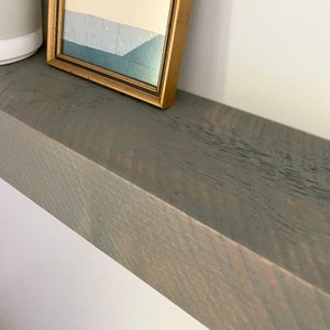 May include: A gray wooden shelf with a gold framed picture on top. The shelf has a rustic, distressed look.