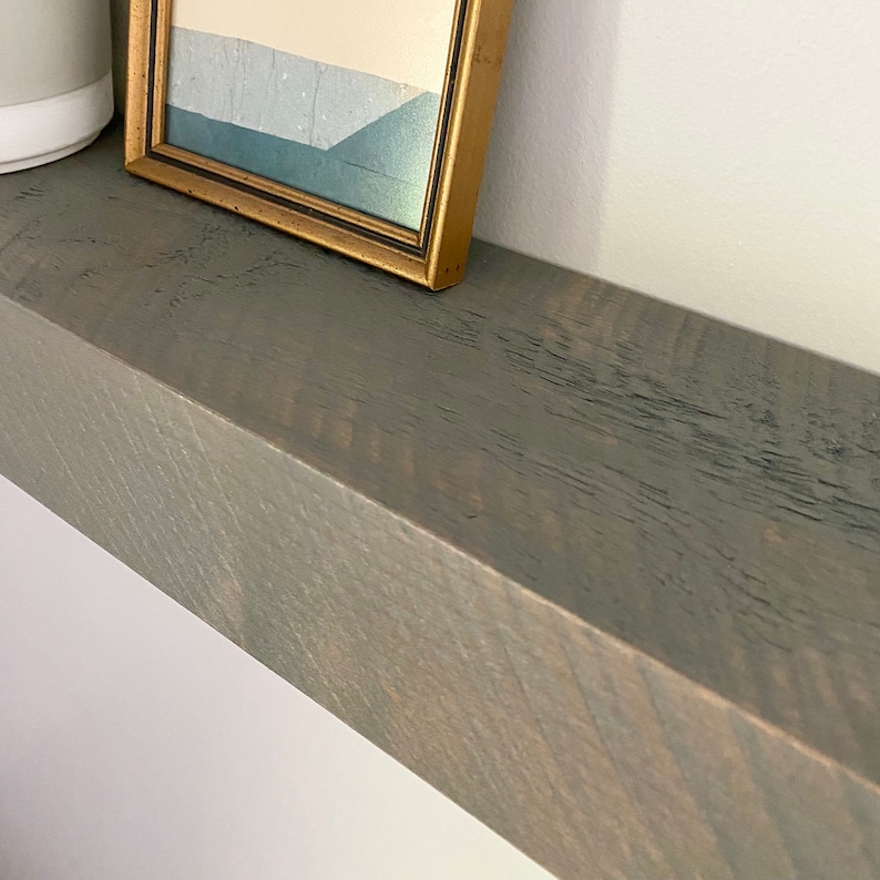 May include: A gray wooden shelf with a gold framed picture on top. The shelf has a rustic, distressed look.