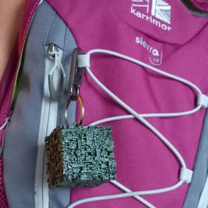 May include: A pink backpack with a gray zipper and white straps. The backpack has a green and brown keychain attached to it. The keychain has the text "sierra 10" on it. The backpack also has the text "karrimor" on it.