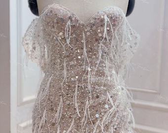 May include: A short, strapless dress with a sweetheart neckline. The dress is covered in sequins and feathers, giving it a glamorous look.