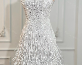 May include: A white, beaded mini dress with a square neckline and spaghetti straps. The dress is covered in small, shimmering beads and has a fringe detail at the hemline. The dress is displayed on a mannequin.