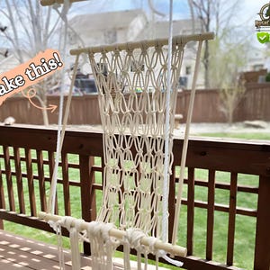 May include: A cream macrame hammock chair with wooden supports hangs on a wooden deck. The text "Make this!" is in a pink and orange bubble. The background includes a green lawn and a wooden fence.