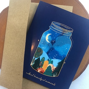 Könnte beinhalten: Eine blaue Karte mit einem goldgeränderten Einmachglas, gefüllt mit einer Nachthimmel-Szene. Das Glas enthält einen Halbmond, Sterne und ein paar Vögel. Der Text "collect beautiful moments" ist in Gold am unteren Rand der Karte geschrieben.