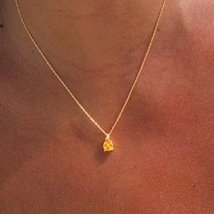 May include: A gold chain necklace with a teardrop-shaped pendant featuring a yellow gemstone.