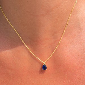 May include: A delicate gold chain necklace with a teardrop-shaped blue gemstone pendant.