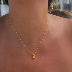 May include: A gold chain necklace with a small, teardrop-shaped pendant. The pendant is a bright yellow colour.