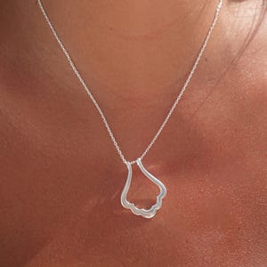 May include: A silver necklace with a delicate, wavy pendant. The pendant is shaped like a teardrop or a cloud.