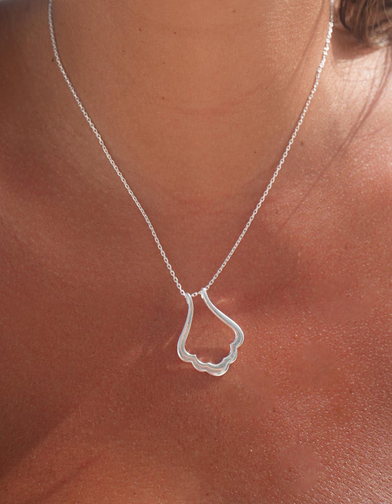 May include: A silver necklace with a delicate, wavy pendant. The pendant is shaped like a teardrop or a cloud.
