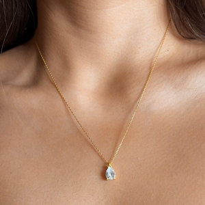 May include: A gold chain necklace with a teardrop-shaped clear crystal pendant.