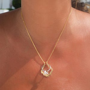 May include: A gold chain necklace with a pendant featuring a double-layered design with a clear gemstone in the center.