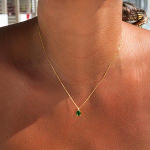 Puede incluir: Un collar de cadena de oro con un colgante de piedra preciosa verde en forma de lágrima.