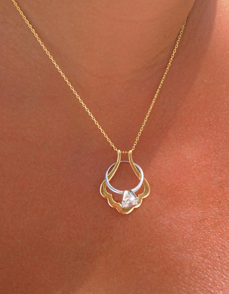 May include: A gold chain necklace with a pendant featuring a ring with a clear gemstone set in a gold and silver setting.