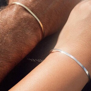 May include: Two simple bracelets, one gold and one silver, worn on the wrists of two people.