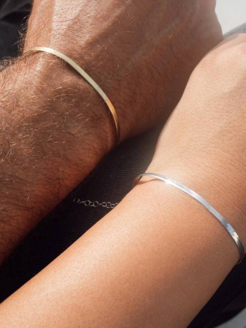 May include: Two simple bracelets, one gold and one silver, worn on the wrists of two people.