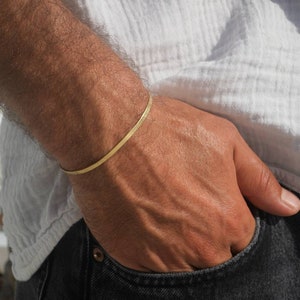 May include: A thin gold bracelet on a person's wrist. The bracelet is simple and minimalist, with a smooth, polished finish.
