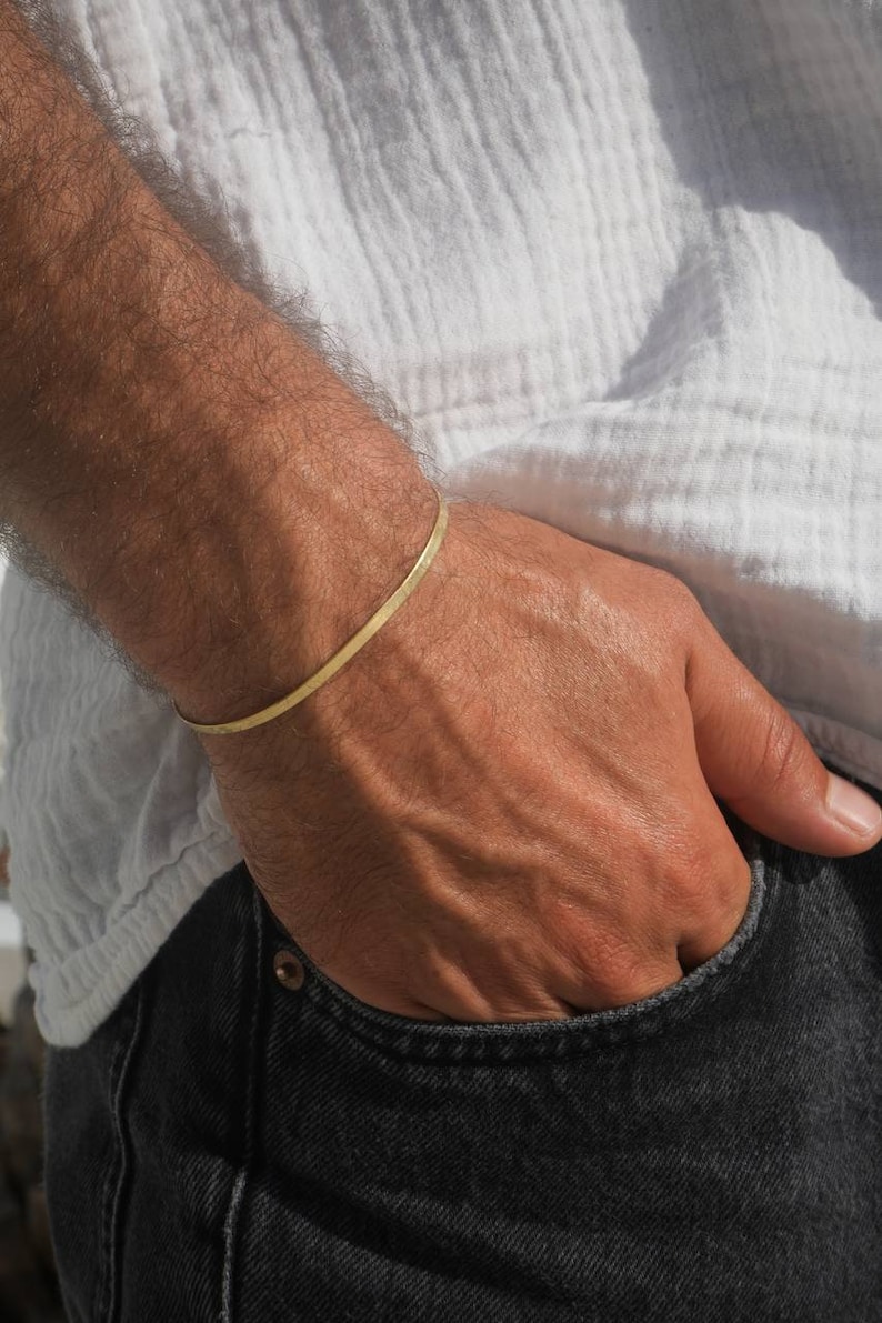 May include: A thin gold bracelet on a person's wrist. The bracelet is simple and minimalist, with a smooth, polished finish.