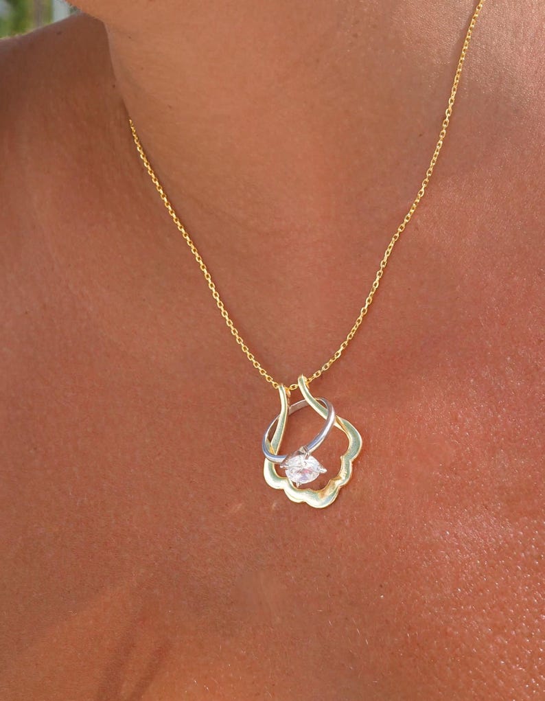 May include: A gold chain necklace with a pendant featuring a clear crystal stone set in a gold and silver ring design.