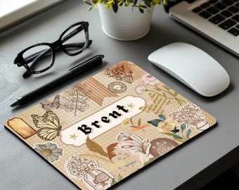 May include: A personalized mousepad with a beige background featuring a grid pattern and floral and butterfly illustrations. The name "Brent" is displayed in a banner. A black pen, glasses, and a computer mouse are also visible.