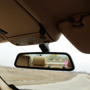 Puede incluir: Un espejo retrovisor con una pegatina de cruz rosa en el cristal.
