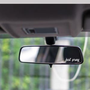 Pode incluir: Um espelho retrovisor com as palavras "just pray" escritas em letras brancas.