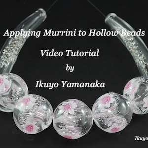 May include: Clear glass beads with pink floral designs are strung together, with curved glass accents at the top. The image includes text that reads "Applying Murrini to Hollow Beads Video Tutorial by Ikuyo Yamanaka."