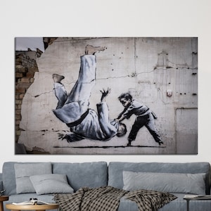May include: A canvas print of a mural depicting a judo match. The artwork shows a figure in a white gi being thrown by a child in a dark outfit. The background is a distressed concrete wall with cracks and exposed brick.