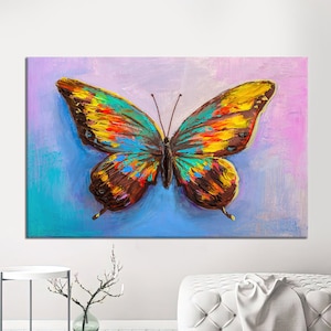 May include: A vibrant, colorful butterfly painting on canvas. The artwork features a large butterfly with wings in shades of yellow, orange, blue, and brown against a blue and purple background. The painting is displayed on a white wall.