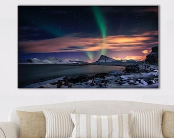 May include: A canvas print showing a night landscape with the aurora borealis. The image depicts a coastal scene with snow-covered rocks and mountains under a starry sky. Green and purple aurora lights illuminate the sky above the mountains.