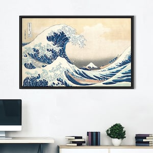 May include: Framed print of "The Great Wave off Kanagawa" by Hokusai. The artwork depicts a large ocean wave with boats and Mount Fuji in the background. The wave is blue and white, set against a beige sky. The print is in a black frame.