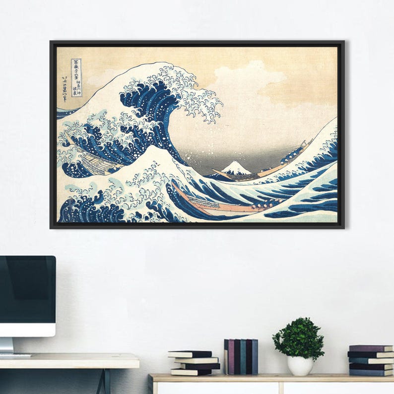 May include: Framed print of "The Great Wave off Kanagawa" by Hokusai. The artwork depicts a large ocean wave with boats and Mount Fuji in the background. The wave is blue and white, set against a beige sky. The print is in a black frame.
