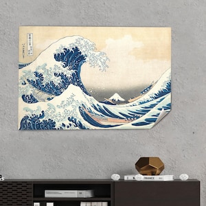 May include: A print of "The Great Wave off Kanagawa" by Hokusai. The artwork depicts a large ocean wave with boats and Mount Fuji in the background. The wave is a deep blue, with white foam and a light beige sky.