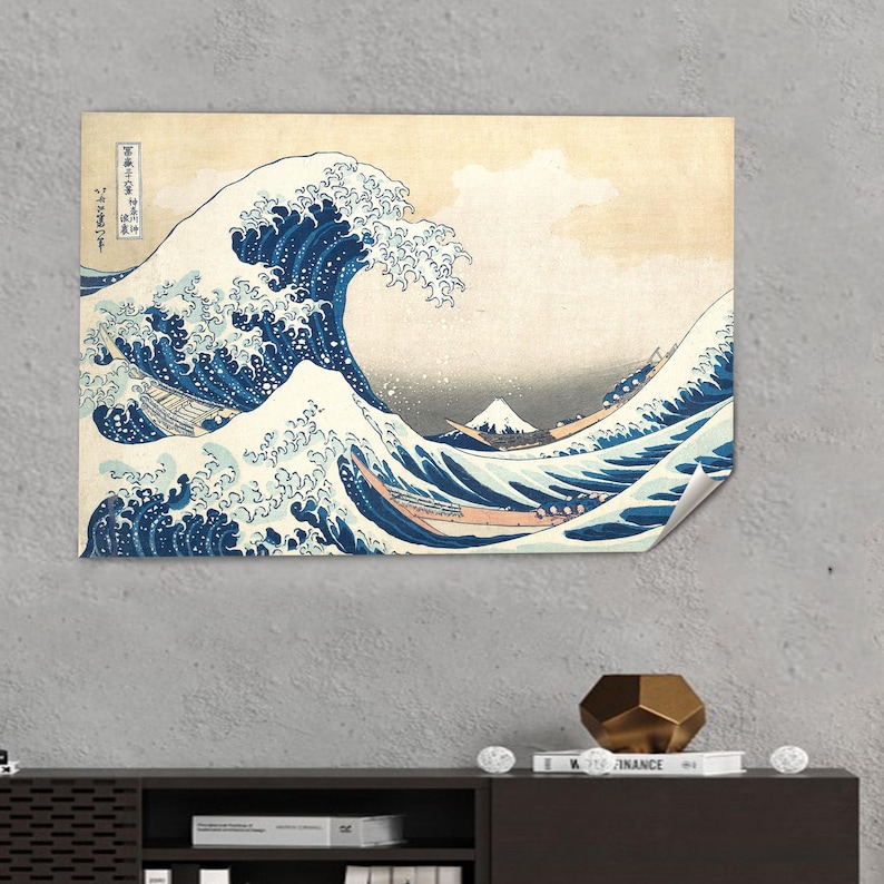 May include: A print of "The Great Wave off Kanagawa" by Hokusai. The artwork depicts a large ocean wave with boats and Mount Fuji in the background. The wave is a deep blue, with white foam and a light beige sky.