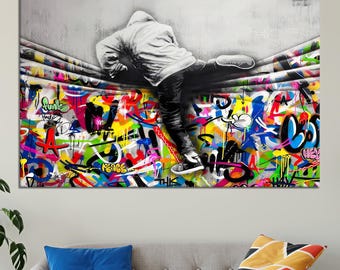 May include: A colorful graffiti wall with a person in a black hoodie and jeans hanging from the wall. The graffiti includes words like "peace", "funk", and "hey".