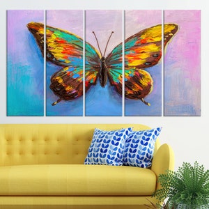 May include: A vibrant, multi-panel canvas art piece featuring a large butterfly. The butterfly's wings are a mix of yellow, orange, blue, and brown, set against a blue and purple background. The artwork is displayed above a yellow sofa with blue patterned pillows.