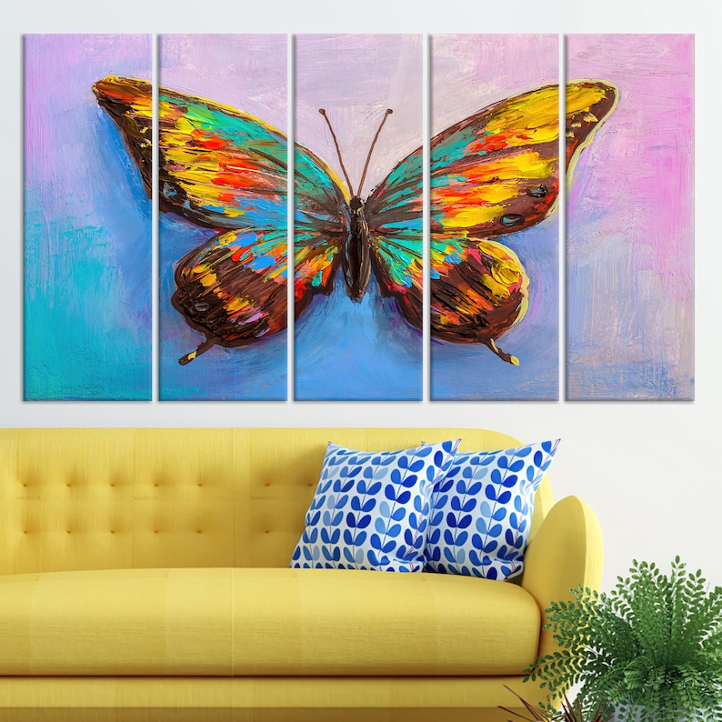 May include: A vibrant, multi-panel canvas art piece featuring a large butterfly. The butterfly's wings are a mix of yellow, orange, blue, and brown, set against a blue and purple background. The artwork is displayed above a yellow sofa with blue patterned pillows.