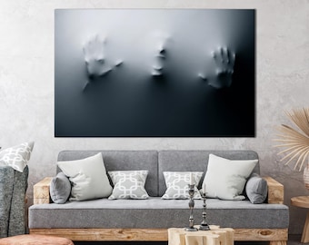 May include: A black and white abstract art print of a face and hands emerging from a textured surface. The print is displayed on a gray wall above a gray couch with pillows.