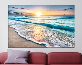 May include: A photograph of a beach scene with a sunrise over the ocean. The waves are crashing on the shore, creating a foamy white edge. The sky is a vibrant orange and pink, with clouds reflecting the light.