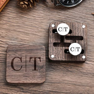 May include: A wooden box with two cufflinks inside. The cufflinks are silver with the initials "C|T" engraved on them. The box is also engraved with the initials "C|T".